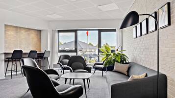 A modern office space with a grey sofa, black chairs, a small table, and a plant.
