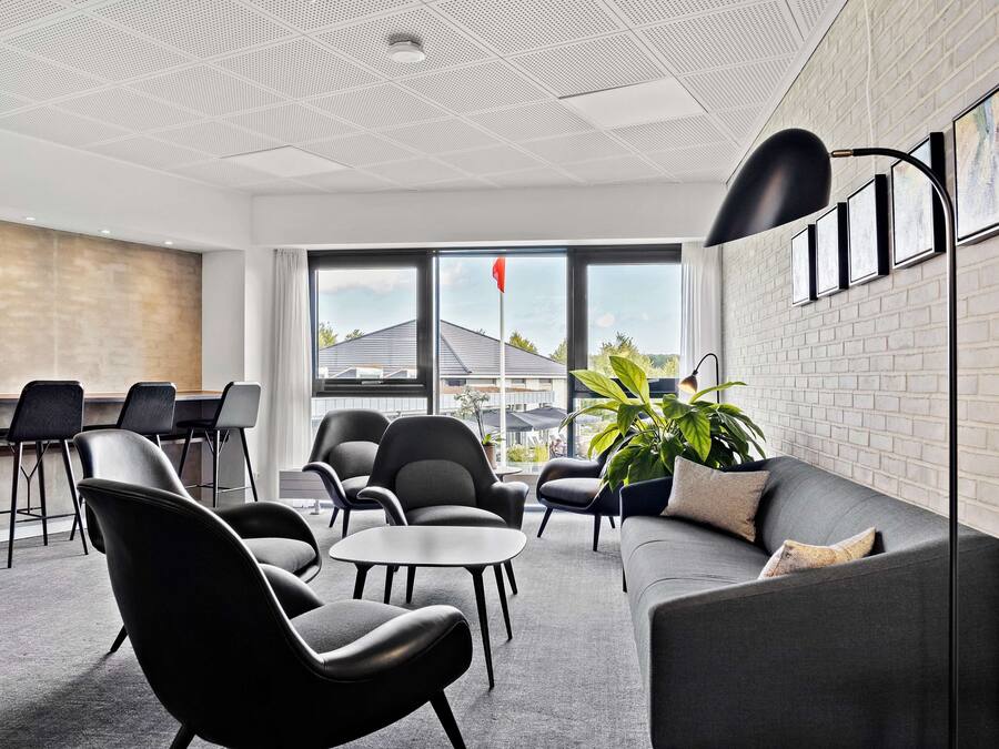 Een moderne kantoorruimte met een grijze bank, zwarte stoelen, een kleine tafel en een plant.