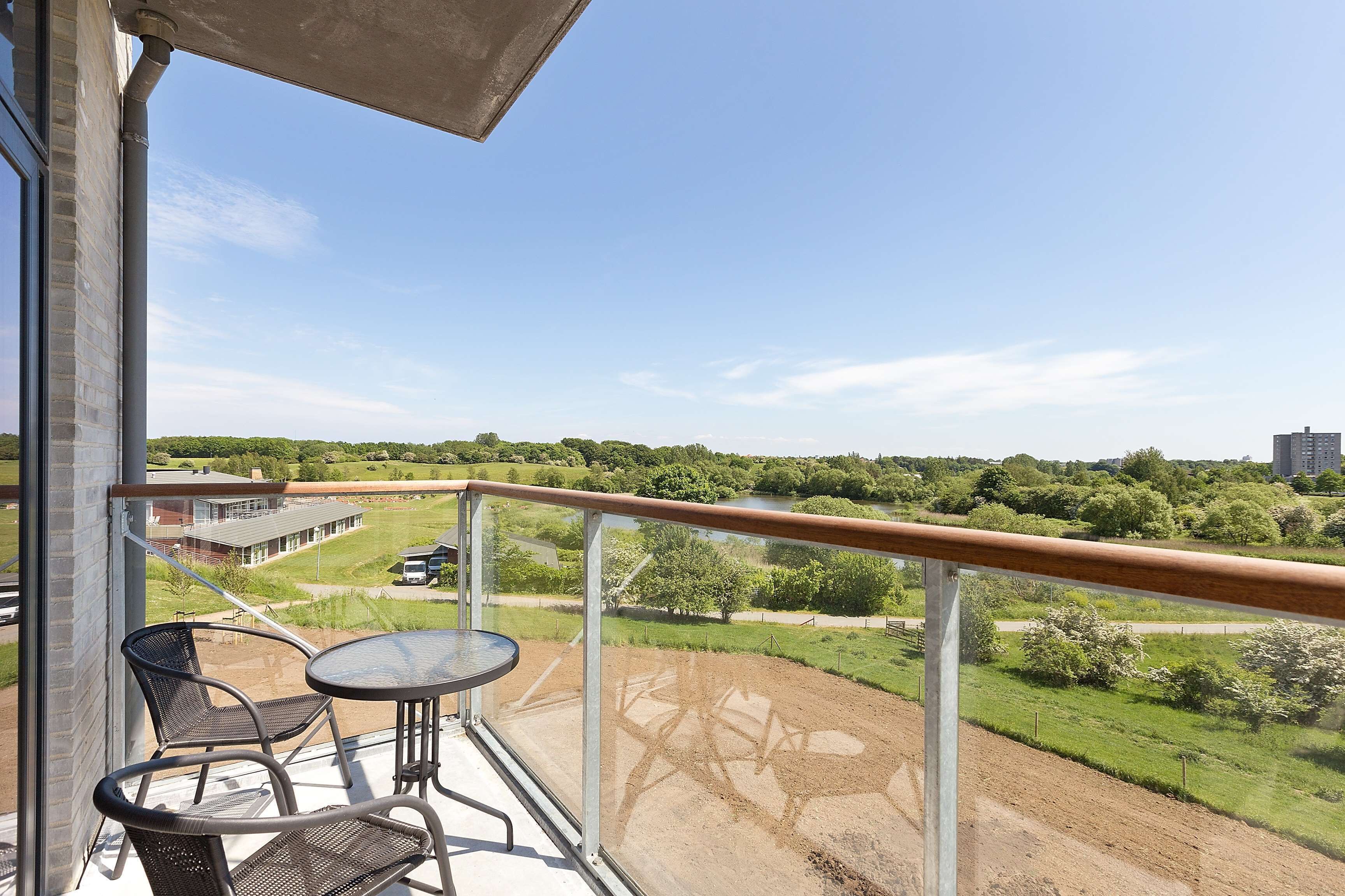 En balkon med et bord og stole, der vender ud mod et grønt landskab og en bygning i det fjerne.