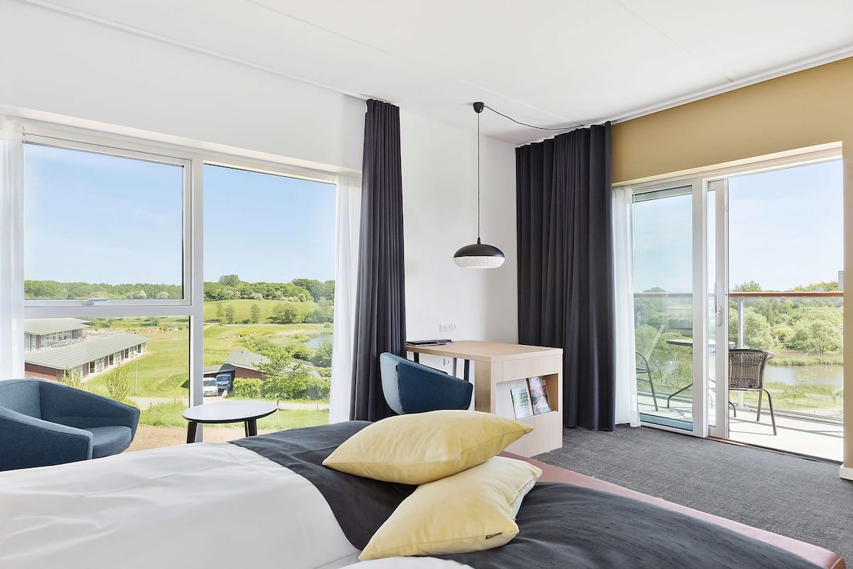 Habitación de hotel con una cama grande, un escritorio y un balcón con vistas al campo.