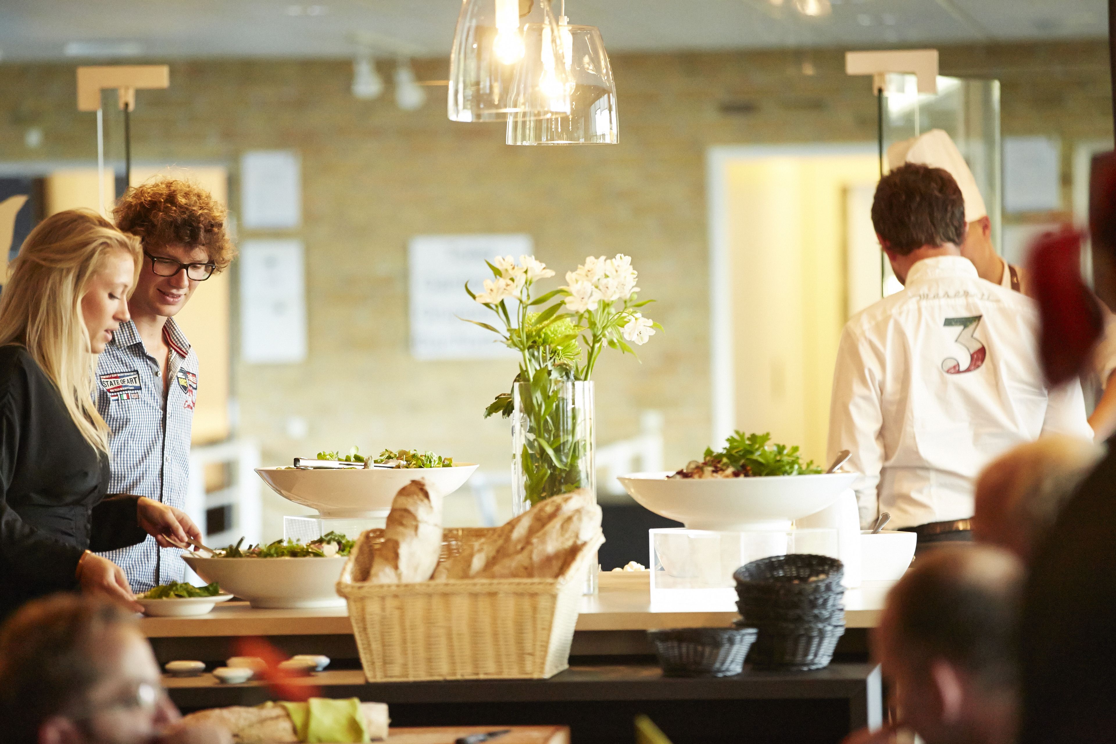 A buffet setup with multiple bowls of food, a vase with flowers, and a chef in a white uniform.