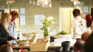 A buffet setup with multiple bowls of food, a vase with flowers, and a chef in a white uniform.