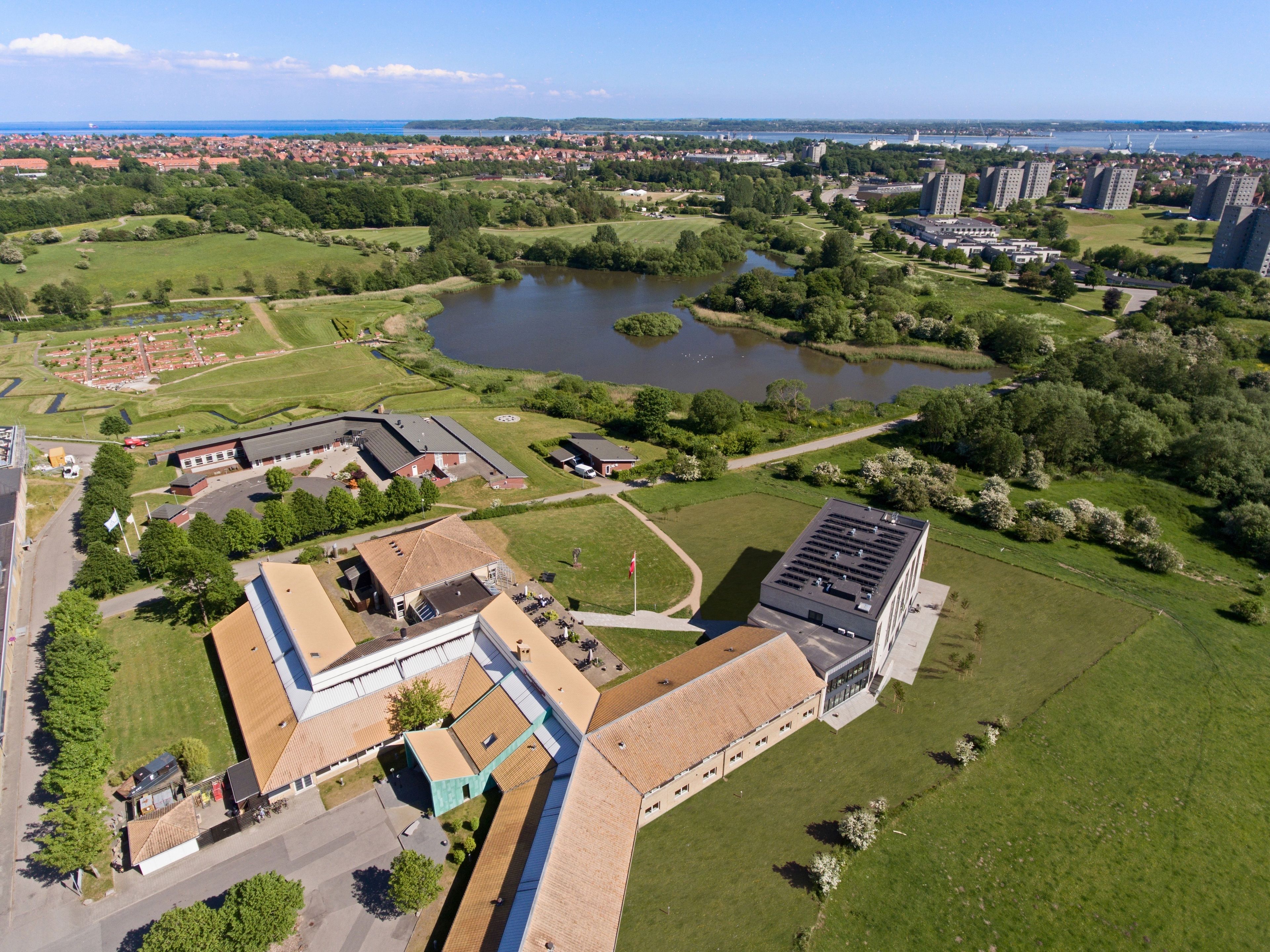 An aerial view of a campus with buildings, green spaces, and a lake.