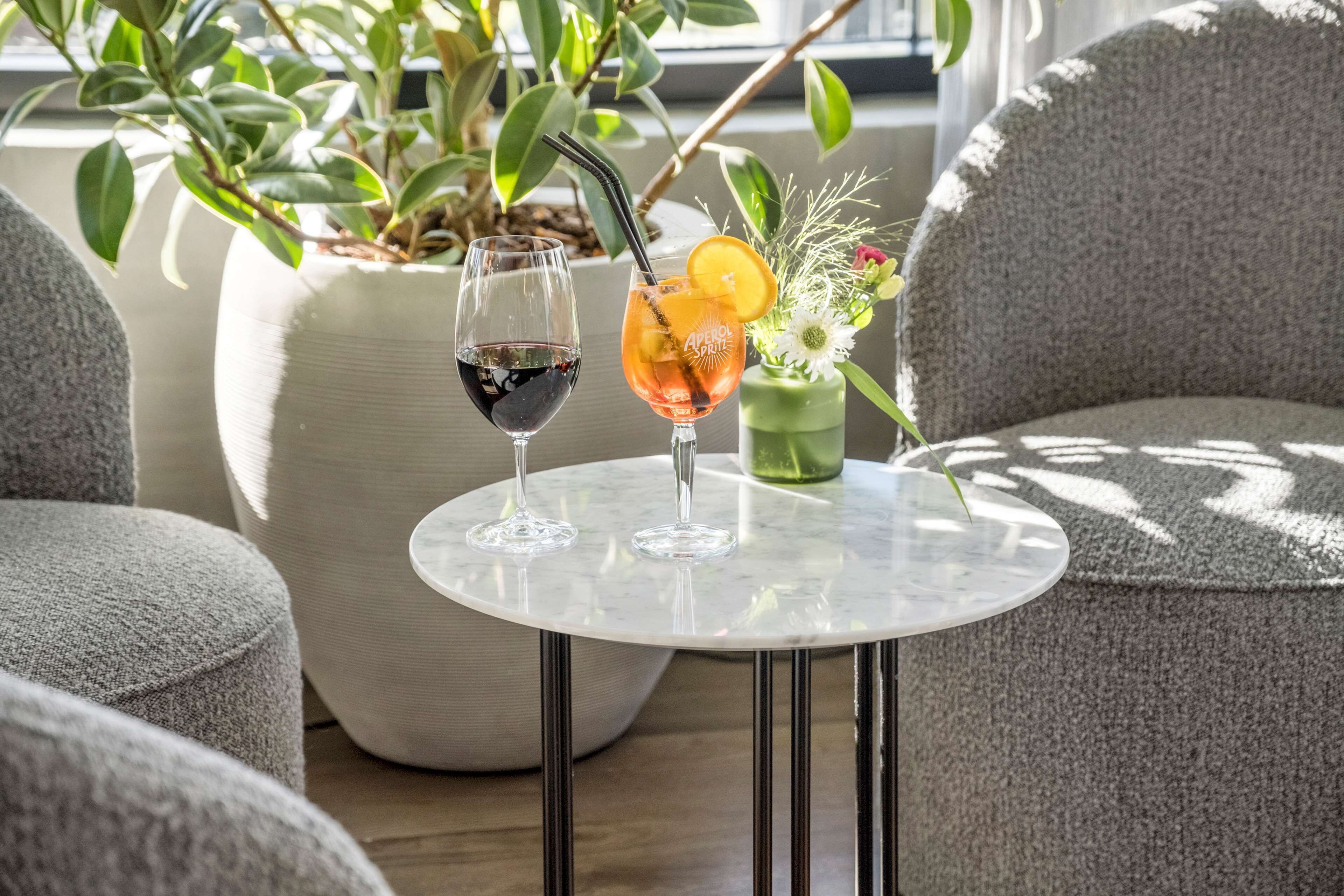 A round table with two glasses of beverages, a potted plant, and a vase with flowers.