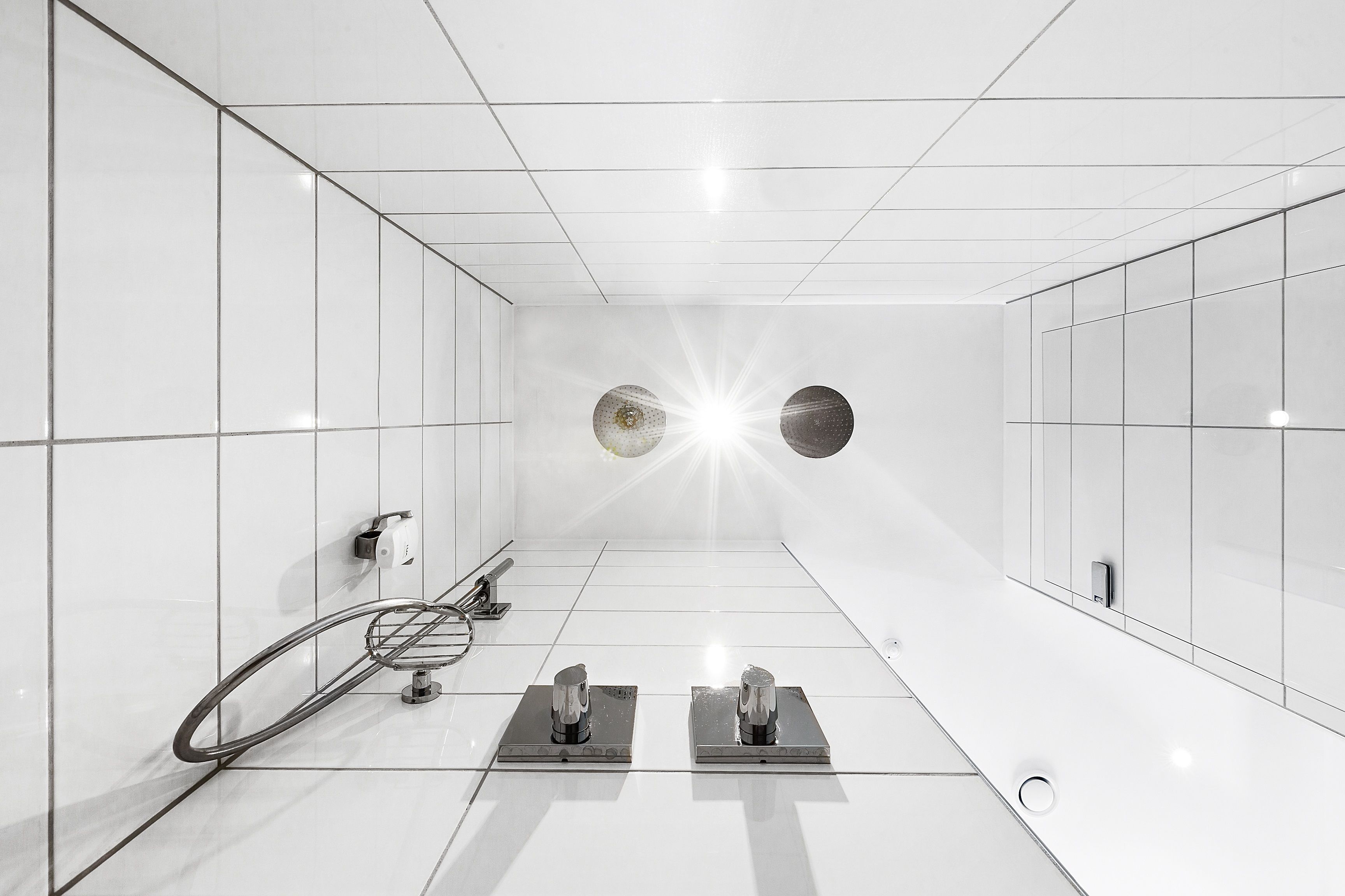 A modern, minimalist bathroom with white tiles, a bicycle rack, and two shower heads.