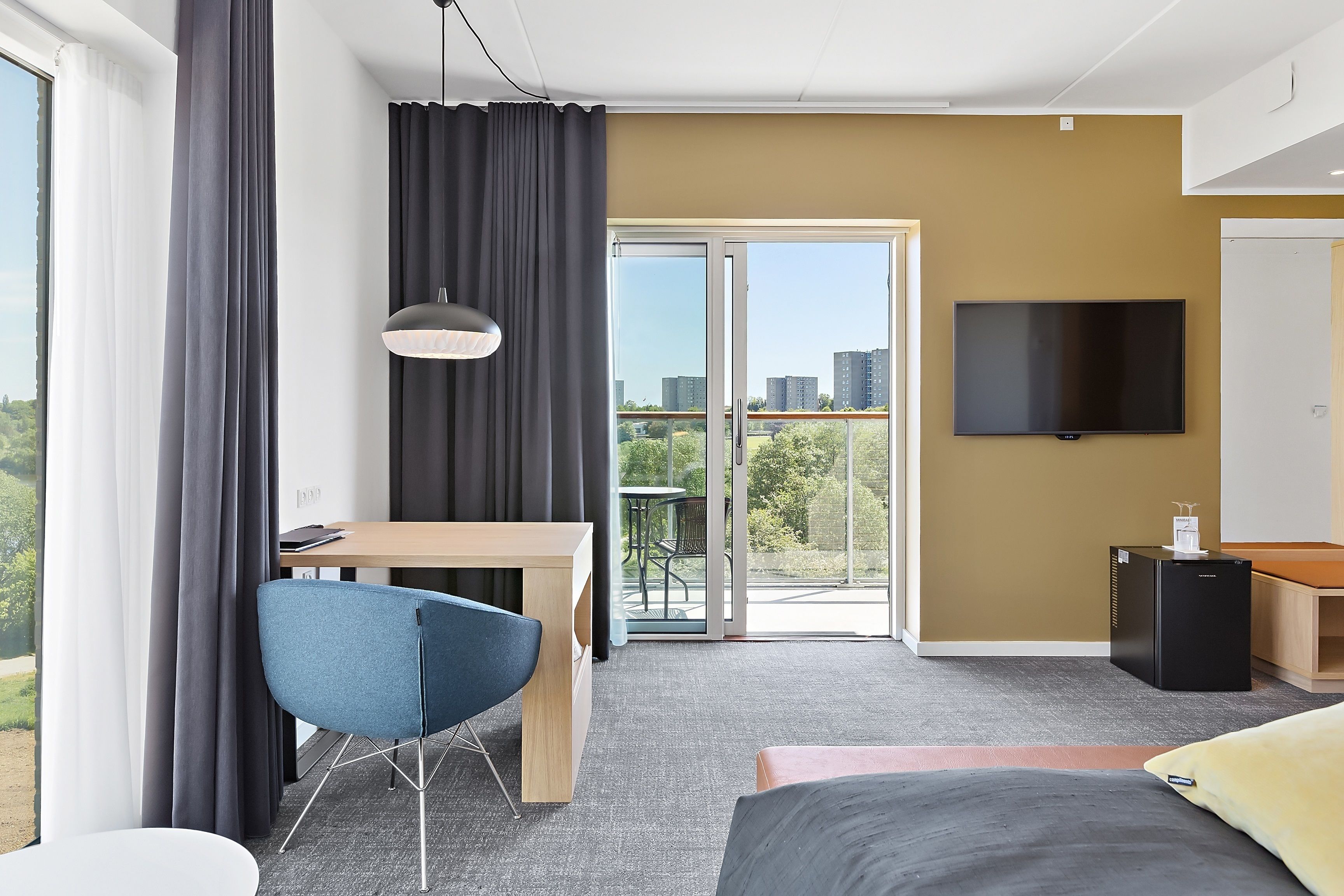 Ein modernes Hotelzimmer mit einem großen Bett, einem Schreibtisch mit Stuhl, einem Flachbildfernseher und einem Balkon mit Blick auf die Stadt.