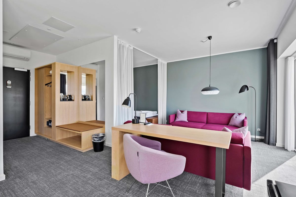 Una habitación moderna con un escritorio de madera, una silla morada, un sofá rojo y una alfombra gris.