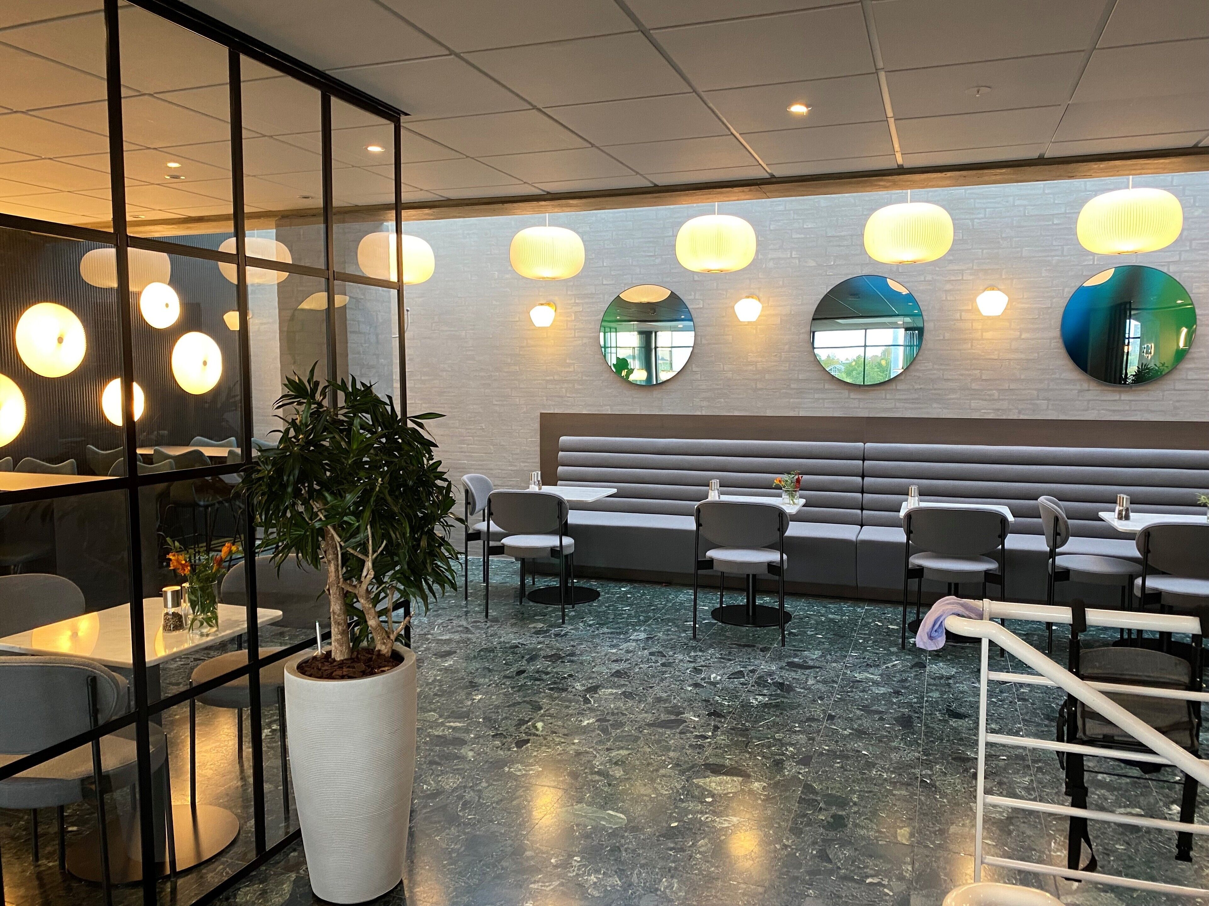 A modern restaurant with a marble floor, seating area with tables and chairs, and decorative wall lights.