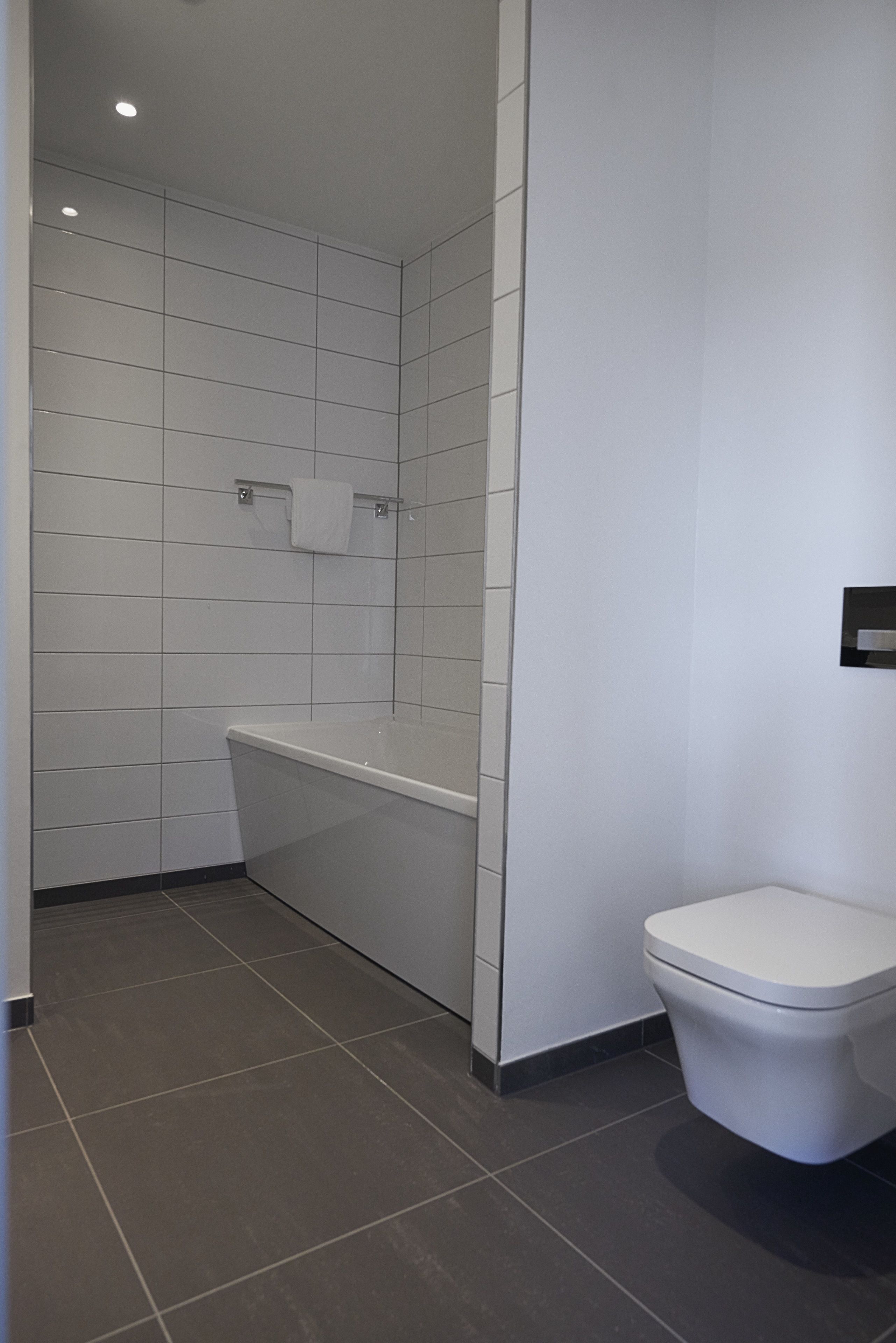 A modern bathroom with white tiles, a bathtub, and a toilet.