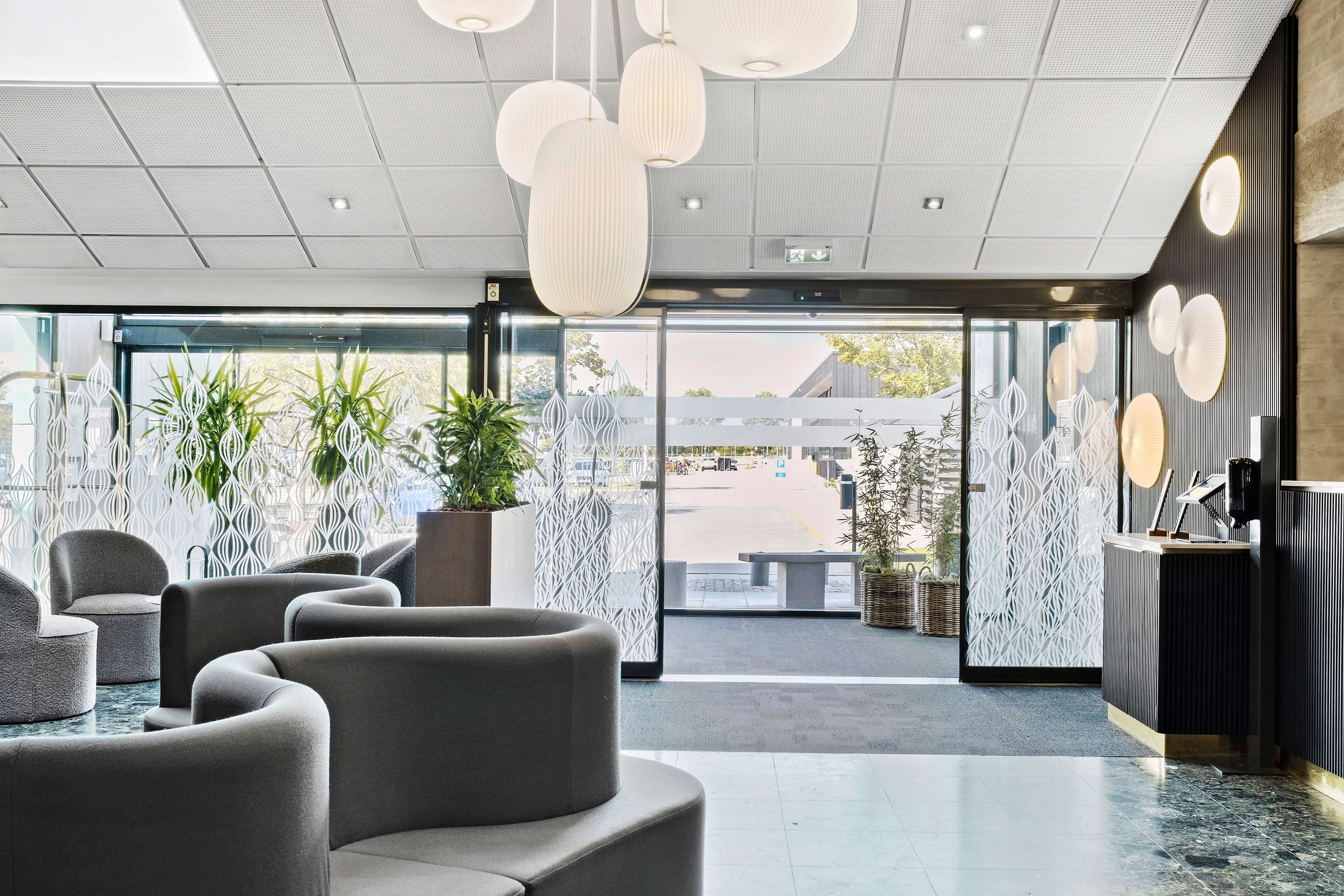 A modern lobby with seating areas, a reception desk, and large windows offering a view of the street.
