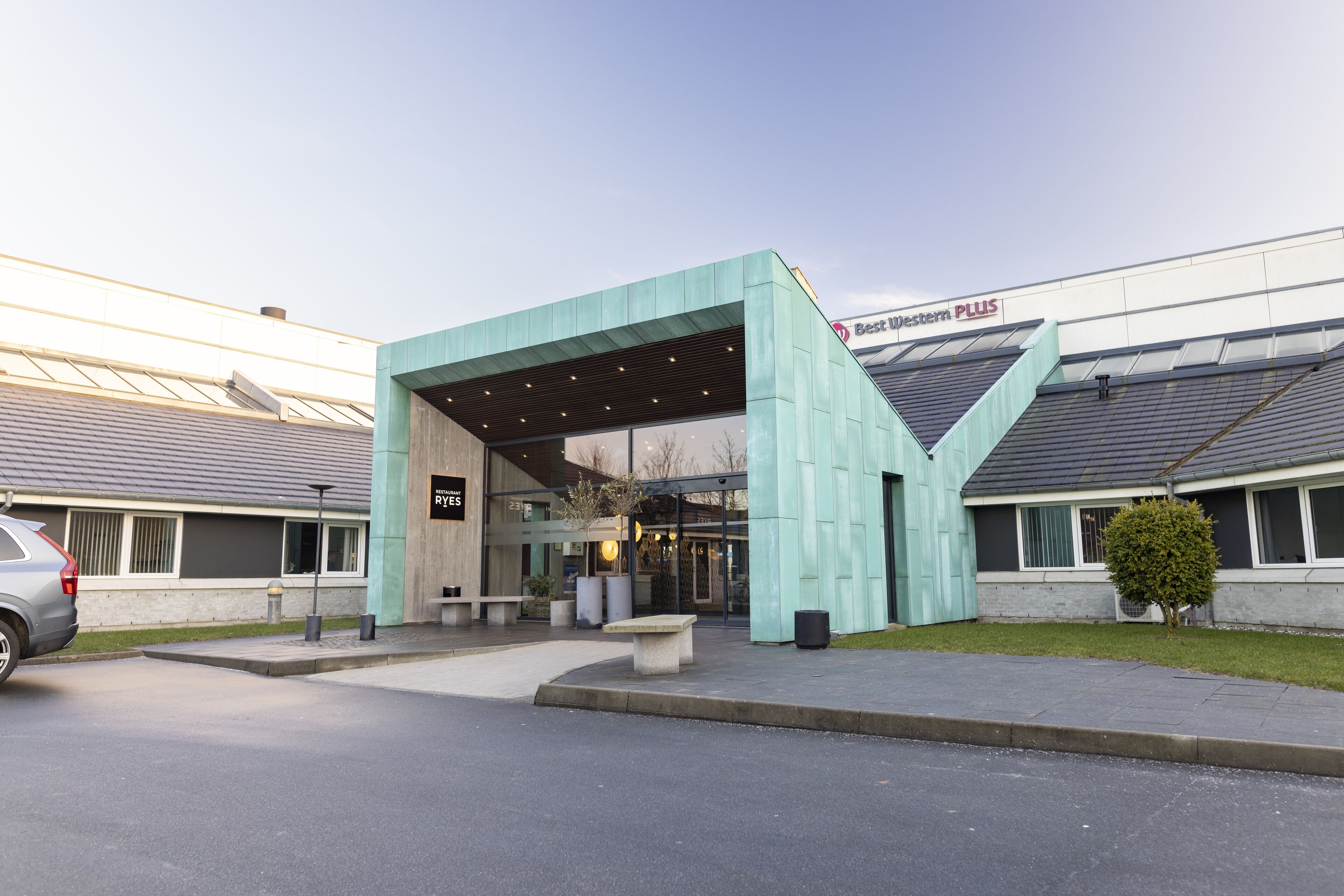 A modern building with a covered entrance, a sign for Best Western PLUS, and a parking area.