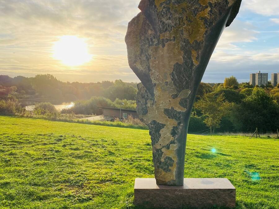 Una scultura in un prato erboso con un tramonto sullo sfondo.
