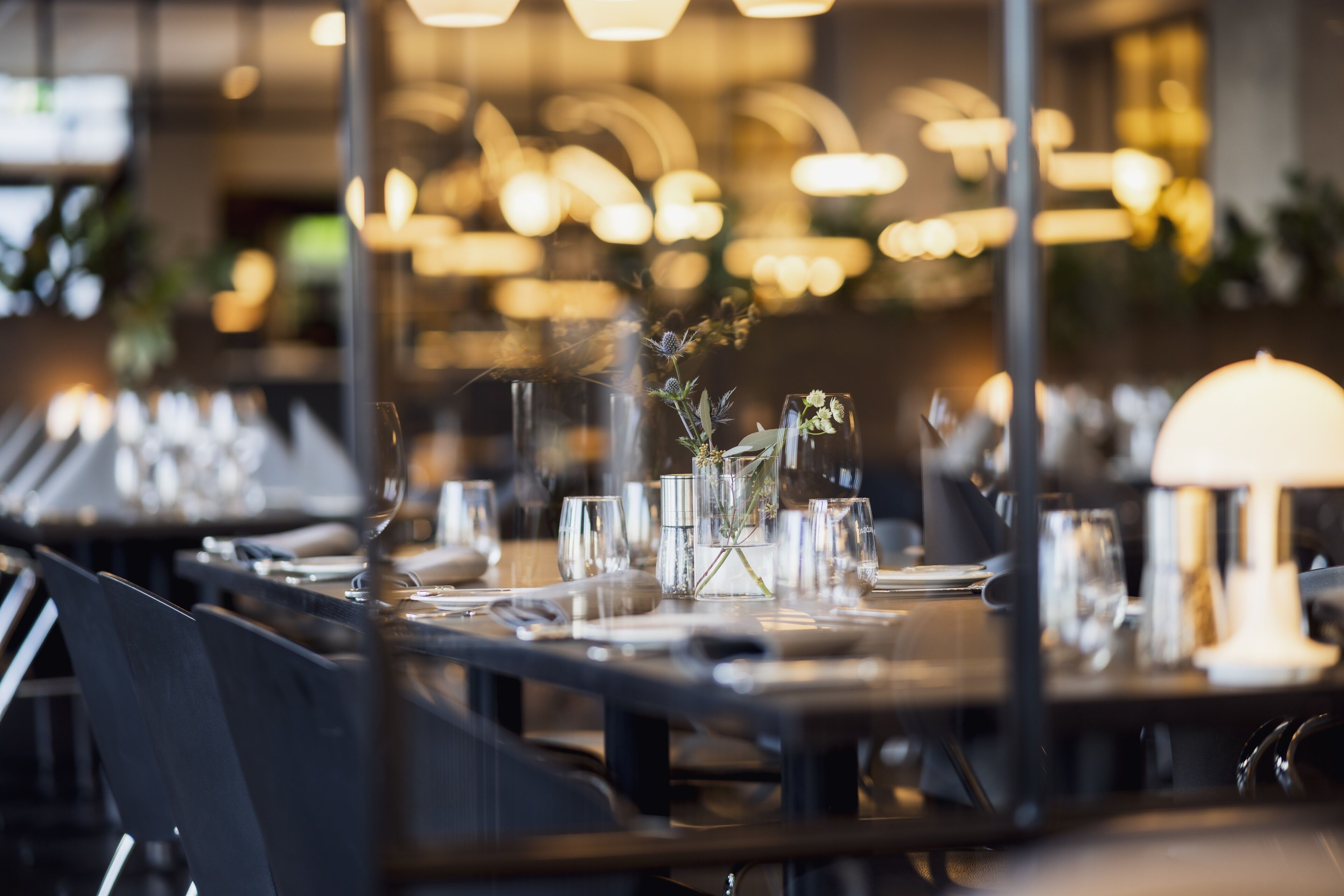 Un ambiente de restaurante con mesas dispuestas para comer, con cristalería y un jarrón con flores.
