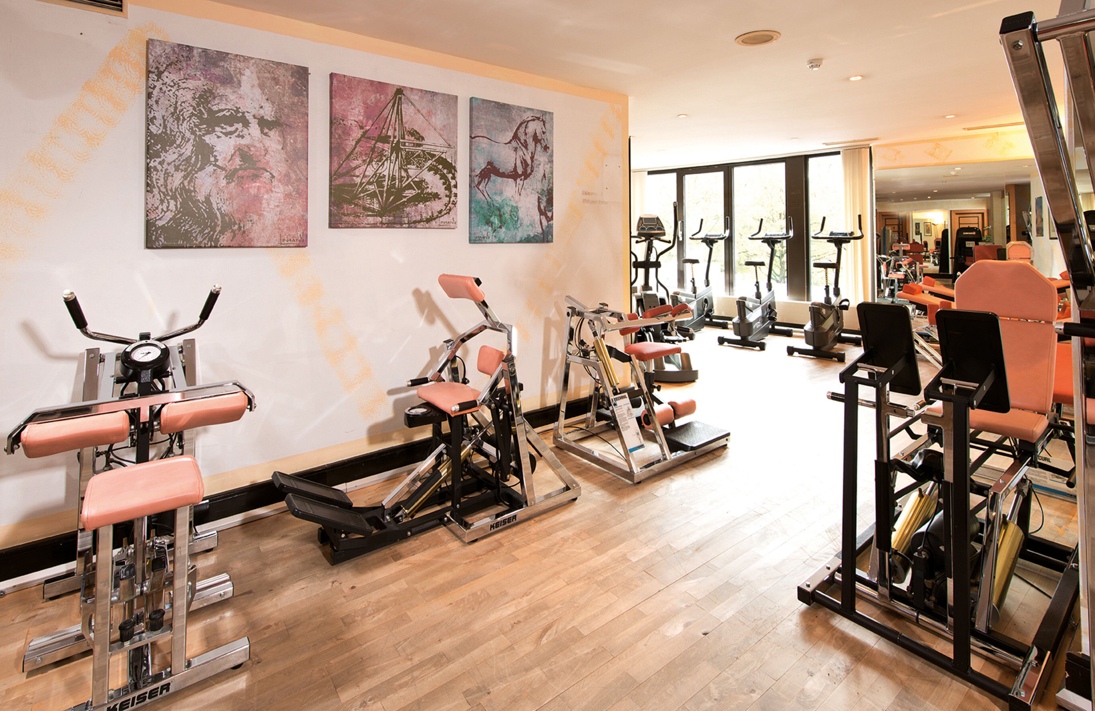 Une salle de sport équipée de divers appareils d’exercice, notamment des tapis de course et des appareils de musculation, et trois tableaux abstraits accrochés au mur.