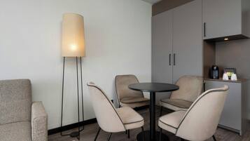 Habitació moderna amb taula rodona, dues cadires, làmpada de peu i zona de cuina equipada.