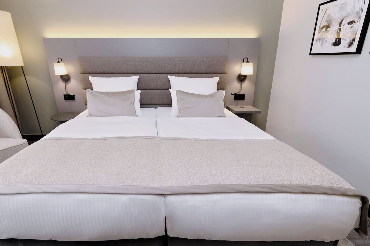 A hotel room with a large bed, two bedside tables, a chair, and a wall-mounted artwork.