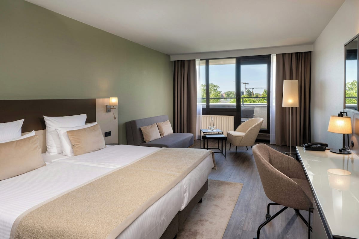 A hotel room with a large bed, a desk, a chair, and a view of the outdoors.