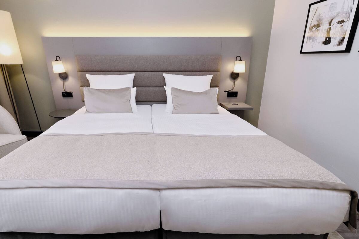 Una habitación de hotel con una cama grande, dos mesitas de noche, una silla y una obra de arte colgada en la pared.