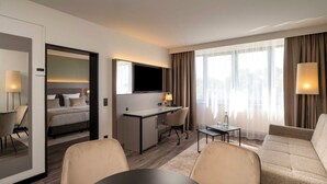 Ein Hotelzimmer mit Bett, Schreibtisch, Bürostuhl, Sofa und Esstisch.