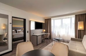 A hotel room with a bed, desk, office chair, sofa, and a dining table. - Leonardo Hotel Hannover (Hannover)