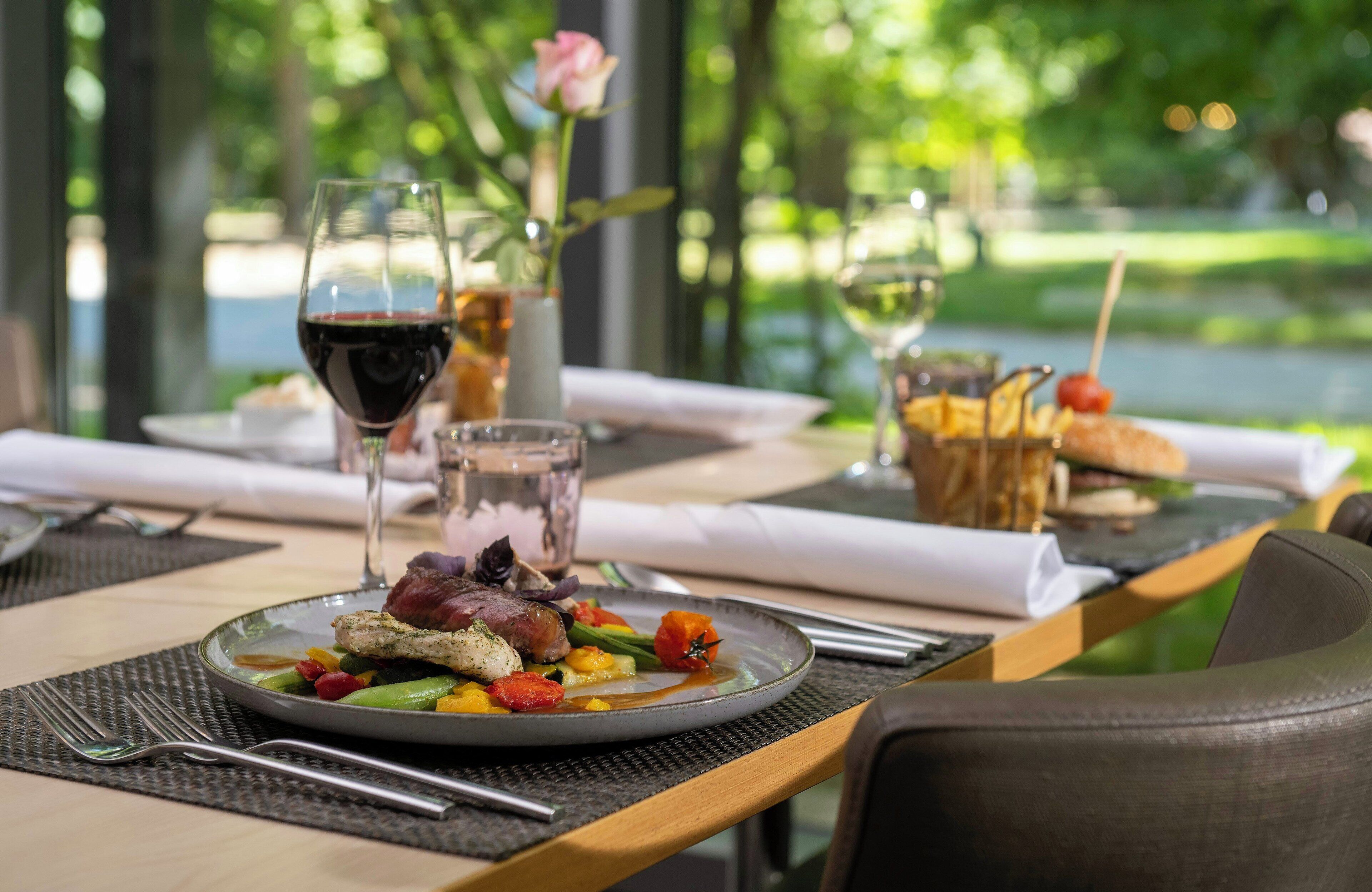 Una mesa de comedor con un plato de comida, copas de vino y un florero con una rosa.