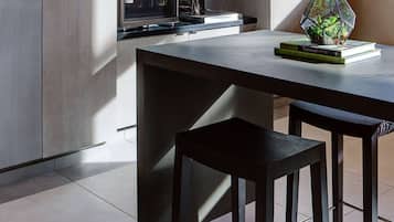 Una cocina moderna con encimera oscura, horno empotrado y vitrina de vidrio. Hay un taburete pequeño y una maceta hexagonal sobre la encimera.