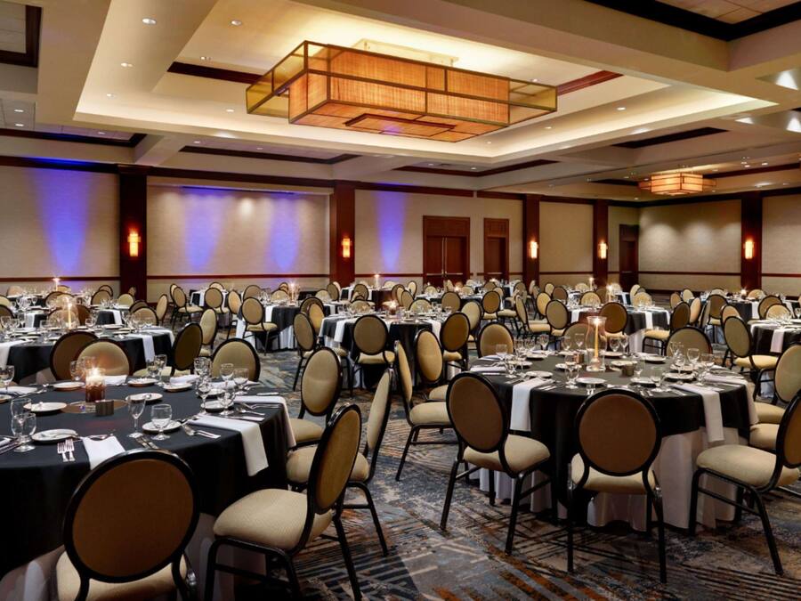 A large banquet hall with multiple round tables set for dining, each with chairs and table settings.