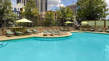 A swimming pool with lounge chairs and umbrellas, surrounded by a stone wall and trees.