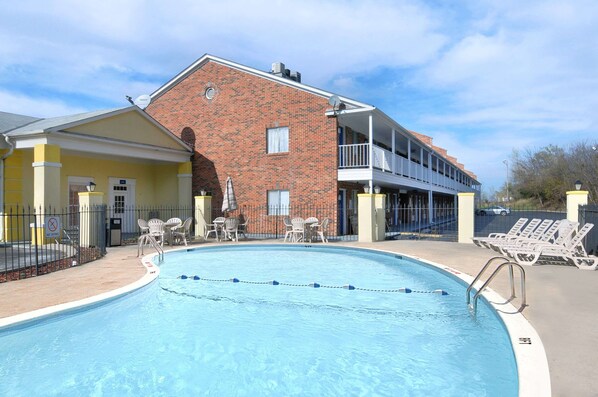 A swimming pool with a brick building in the background, outdoor seating, and a covered area with a balcony. - Days Inn by Wyndham KU Lawrence (Lawrence)