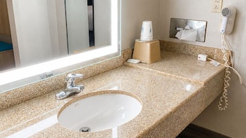 Une salle de bain avec un comptoir en granit, un lavabo blanc, un miroir, un sèche-cheveux et une boîte de mouchoirs.