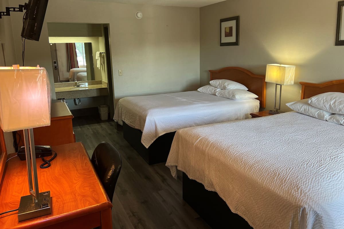 Une chambre d’hôtel avec deux lits, un bureau avec une lampe, un miroir et un tableau au mur.