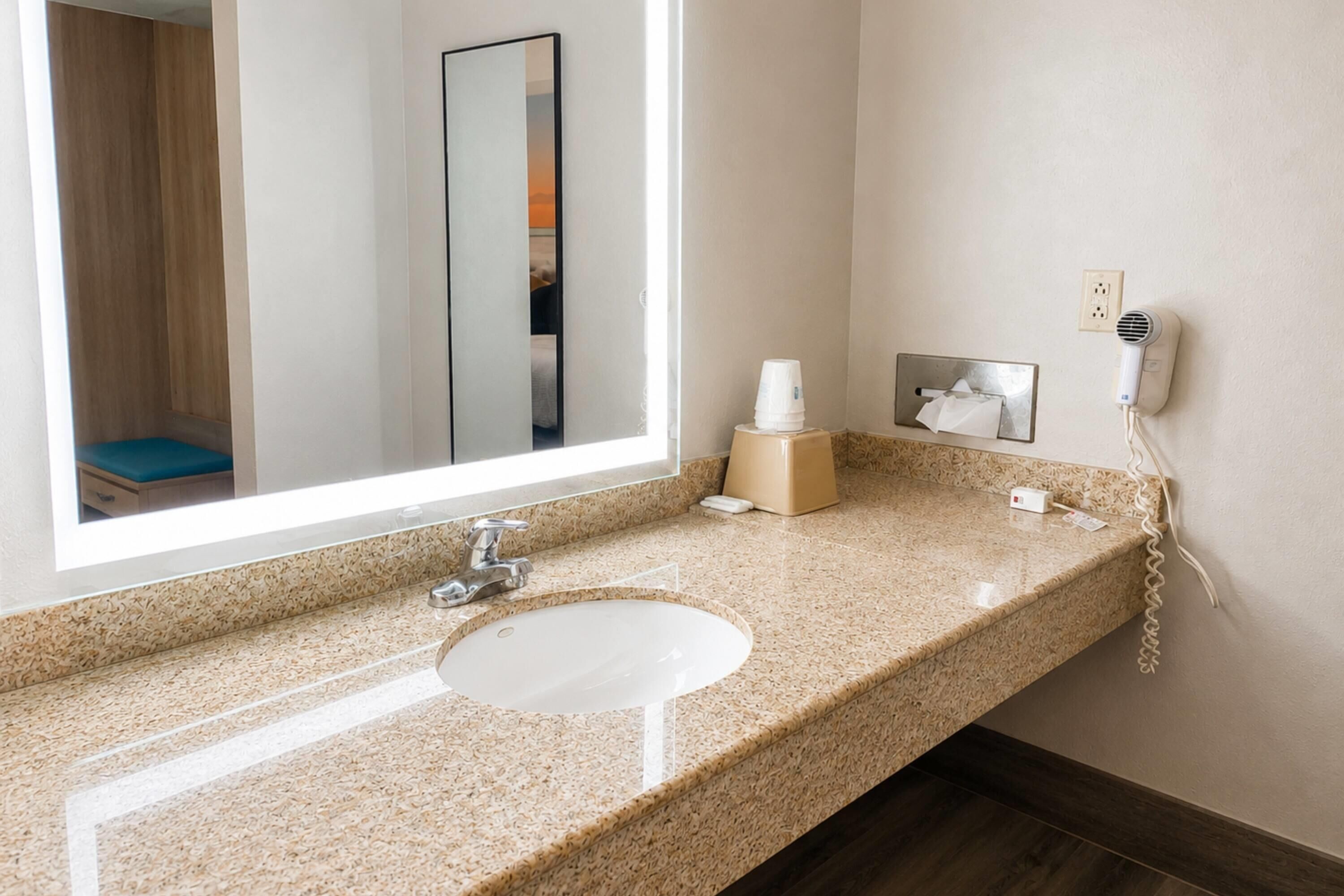 A bathroom with a sink, mirror, and a hairdryer on the wall.