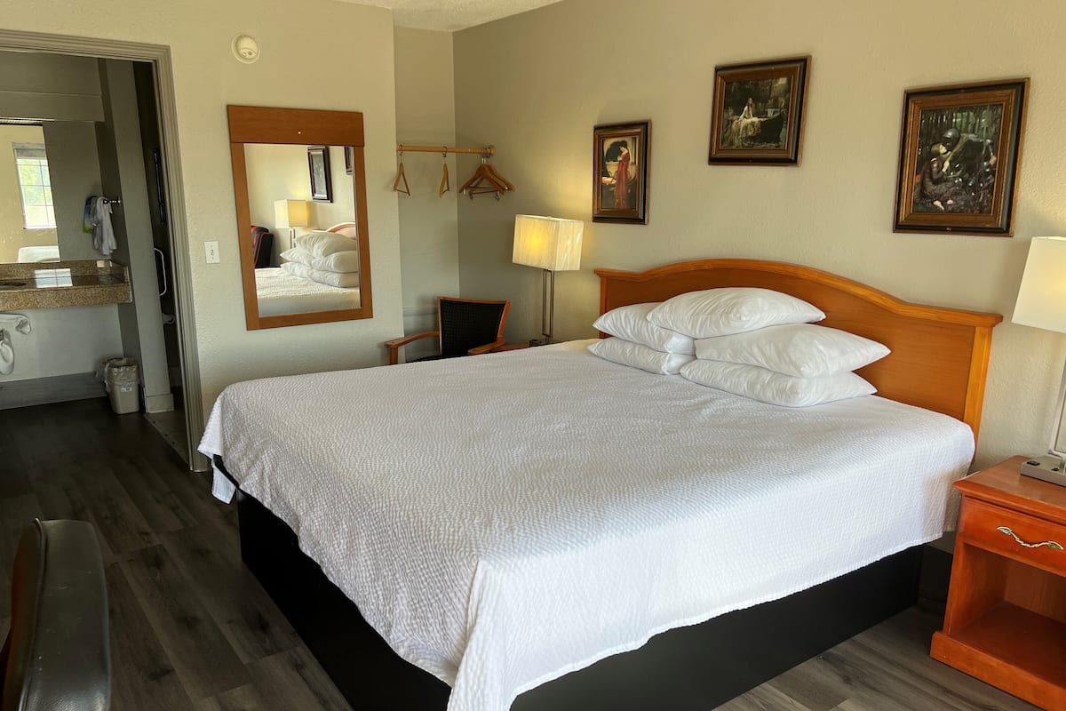 Une chambre d’hôtel avec un grand lit, une tête de lit en bois, une table de chevet avec une lampe, un miroir et un porte-manteau fixé au mur.