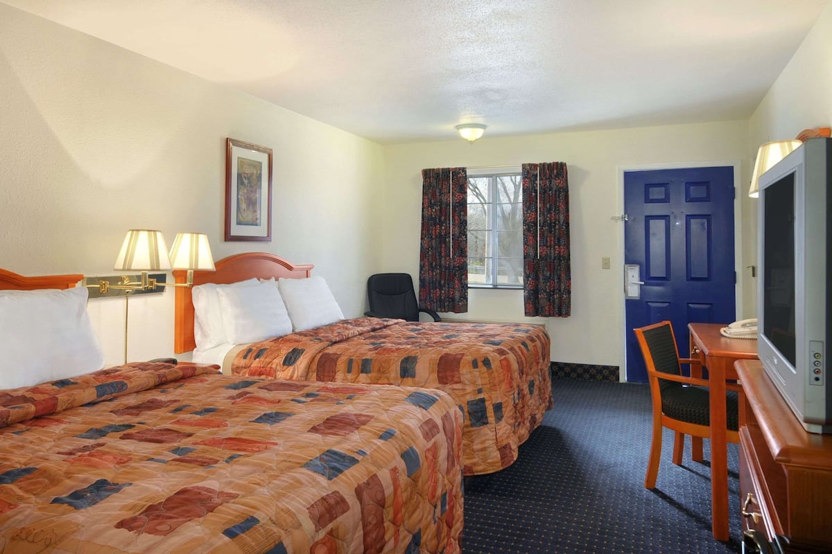 Une chambre d’hôtel avec deux lits, un bureau avec une télévision et une chaise.