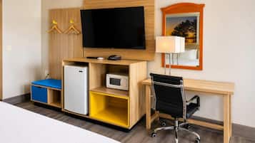Habitación de hotel con cama, escritorio con silla, televisor, refrigerador, microondas y lámpara.