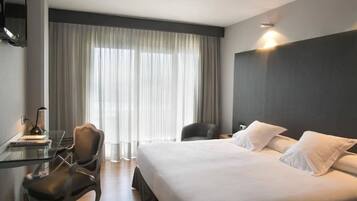 A hotel room with a large bed, a desk with a chair, a television, and a window with curtains.
