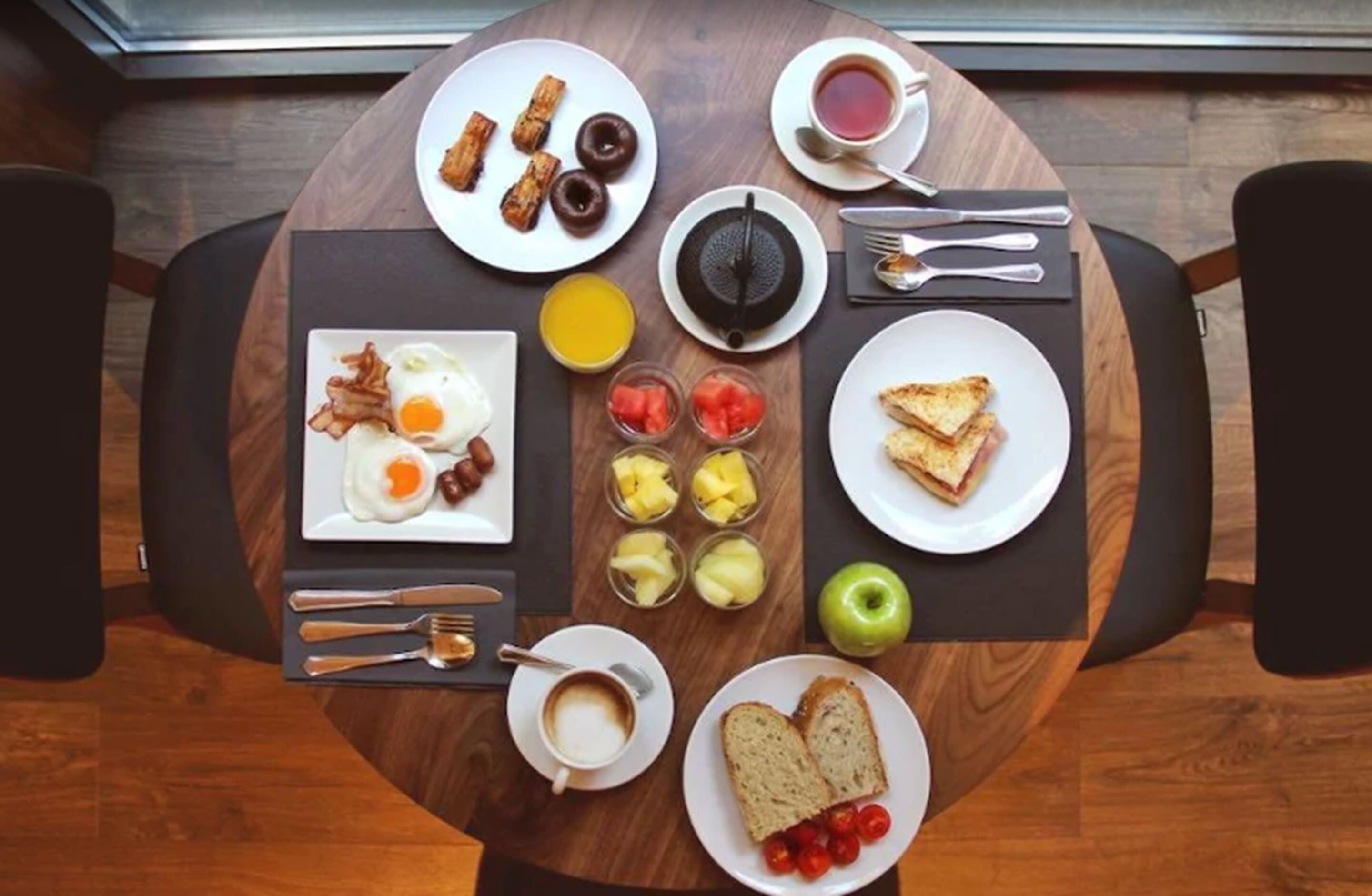 Una mesa de desayuno con platos de huevos, tocino, tostadas y fruta.