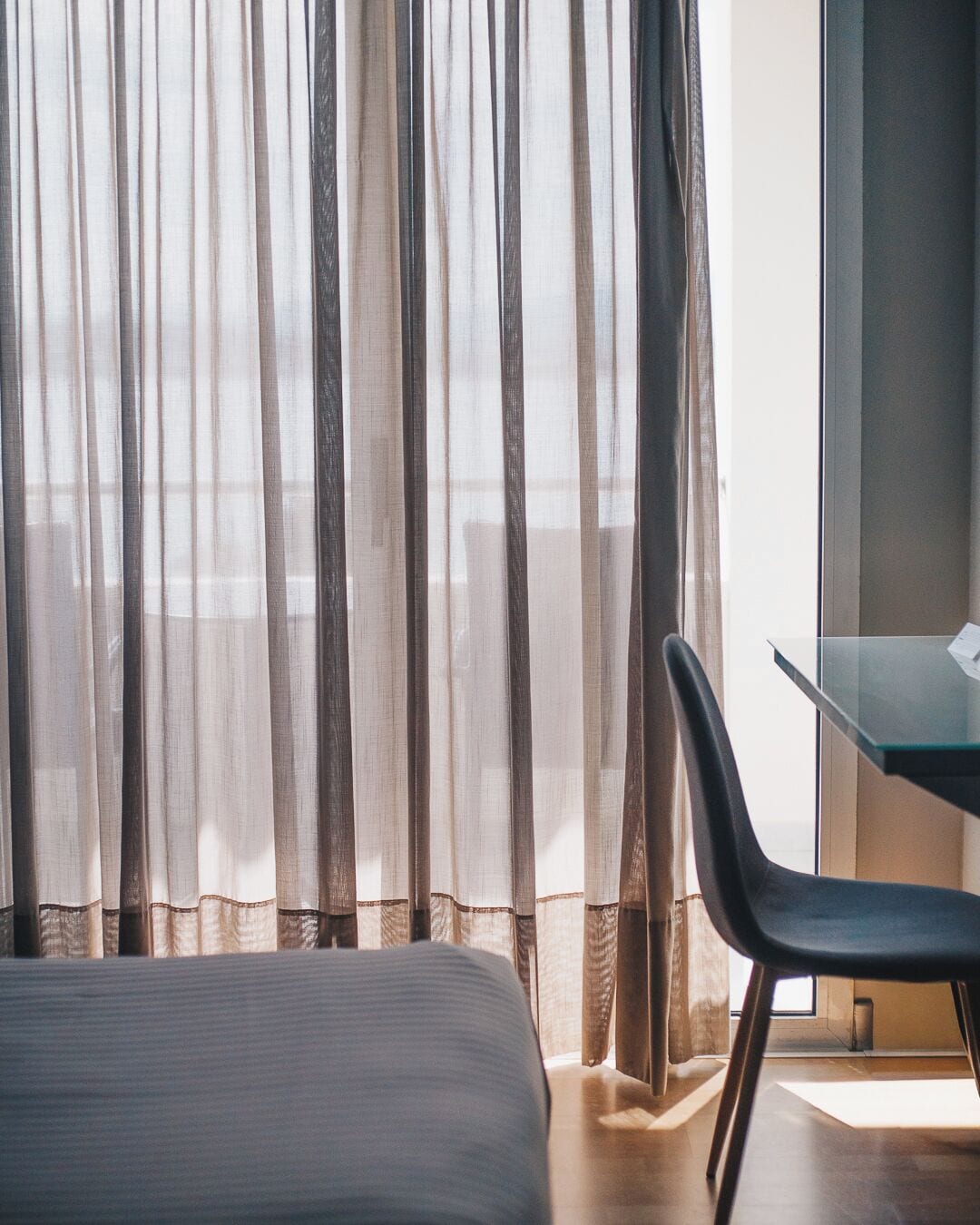 Una habitación de hotel con cama, una silla y cortinas translúcidas.