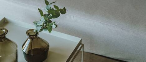 Una sala de estar moderna con un sofá, cojines, una mesa de centro con jarrones de vidrio y una planta.