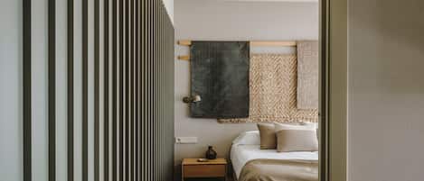 Un pasillo estrecho que conduce a un dormitorio con cama, mesita de noche y una lámpara de pared.