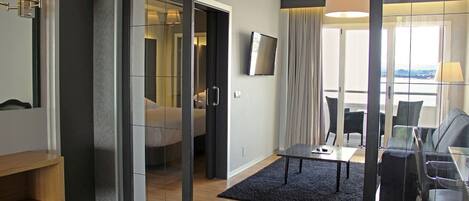 A modern hotel room with a large bed, a TV, a seating area with a table and chairs, and a view of the outdoors.