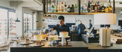 A modern bar with a counter displaying various desserts and bottles of liquor.