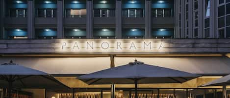 A building with a sign reading "PANORAMA" and outdoor seating with umbrellas.