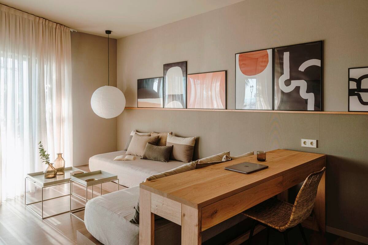 Un dormitorio moderno con cama, un escritorio de madera y una silla. Hay pinturas abstractas en la pared y una ventana grande con cortinas.