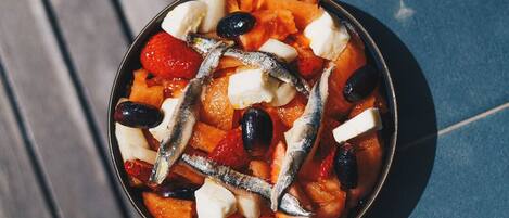 A bowl of fruit salad with olives and anchovies on a table.