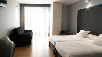 Habitación de hotel con dos camas, un sofá, una silla y un ventanal grande con cortinas.