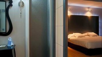 Una habitación de hotel moderna con una cama grande, una mesita de noche, un espejo y una lámpara fijada a la pared.