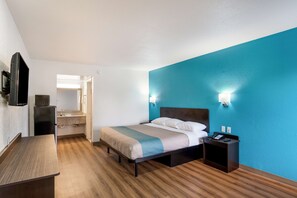 A hotel room with a bed, bedside table, nightstand, and a small desk area.