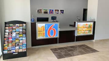 Uma área de recepção de hotel com um grande sinal do número 6, um visor digital com uma mensagem e uma máquina de venda automática com diversos itens.