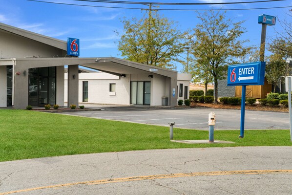 A 6 Lobby hotel entrance with a clear driveway and a parking lot.